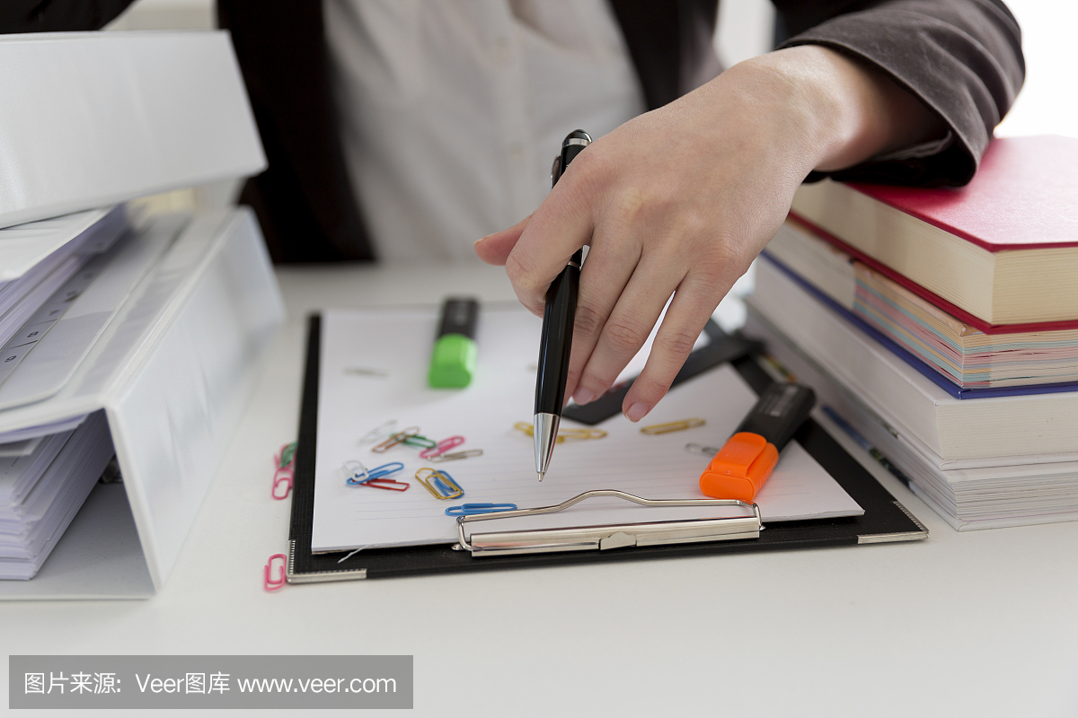 坐在滿是文書,書籍和文件的桌子旁的女人?；靵y的工作場所。過載和過度勞累